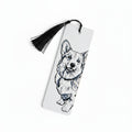 A white rectangular bookmark with a black tassel, featuring a black line art sketch of a corgi dog on the front, photographed against a light beige textured background.