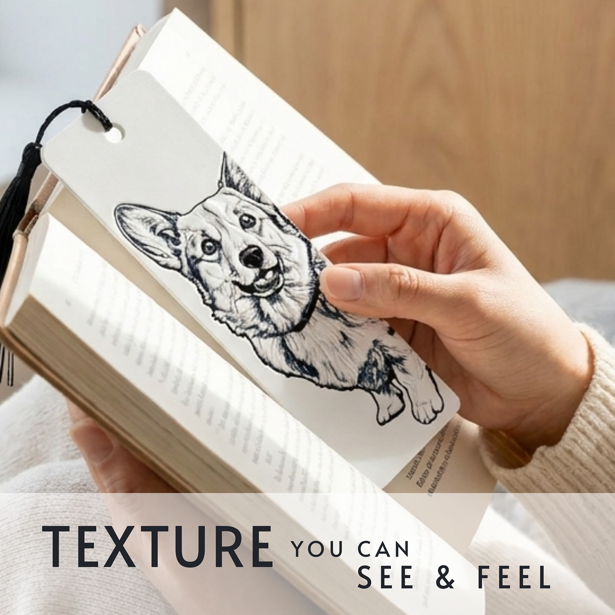 A close-up of a hand holding an open book, with a bookmark shaped like a corgi dog illustration attached to the page. The bookmark has a black line drawing of a corgi on a white textured background, and the text 'TEXTURE YOU CAN SEE & FEEL' appears at the bottom.
