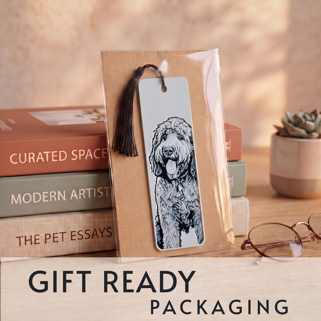 A packaged bookmark featuring a black-and-white illustration of a curly-haired dog, displayed upright on stacked books with a tassel. The scene includes a small potted succulent and eyeglasses on a wooden surface, with the text 'GIFT READY PACKAGING' at the bottom.