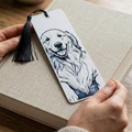 A white rectangular bookmark with a black line drawing of a smiling dog and a black tassel, held by two hands over a beige textured book.