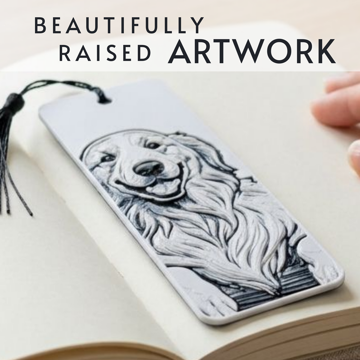 A rectangular bookmark with a raised black-and-white portrait of a dog, shown resting on an open book. A black tassel hangs from the top, and a hand is partially visible at the right edge.