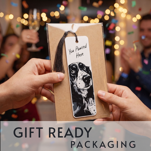 A gift-ready bookmark in kraft paper packaging with a black tassel, held by two hands. The bookmark has a white label featuring a black-and-white dog illustration and the text 'You Pawsed Here'.