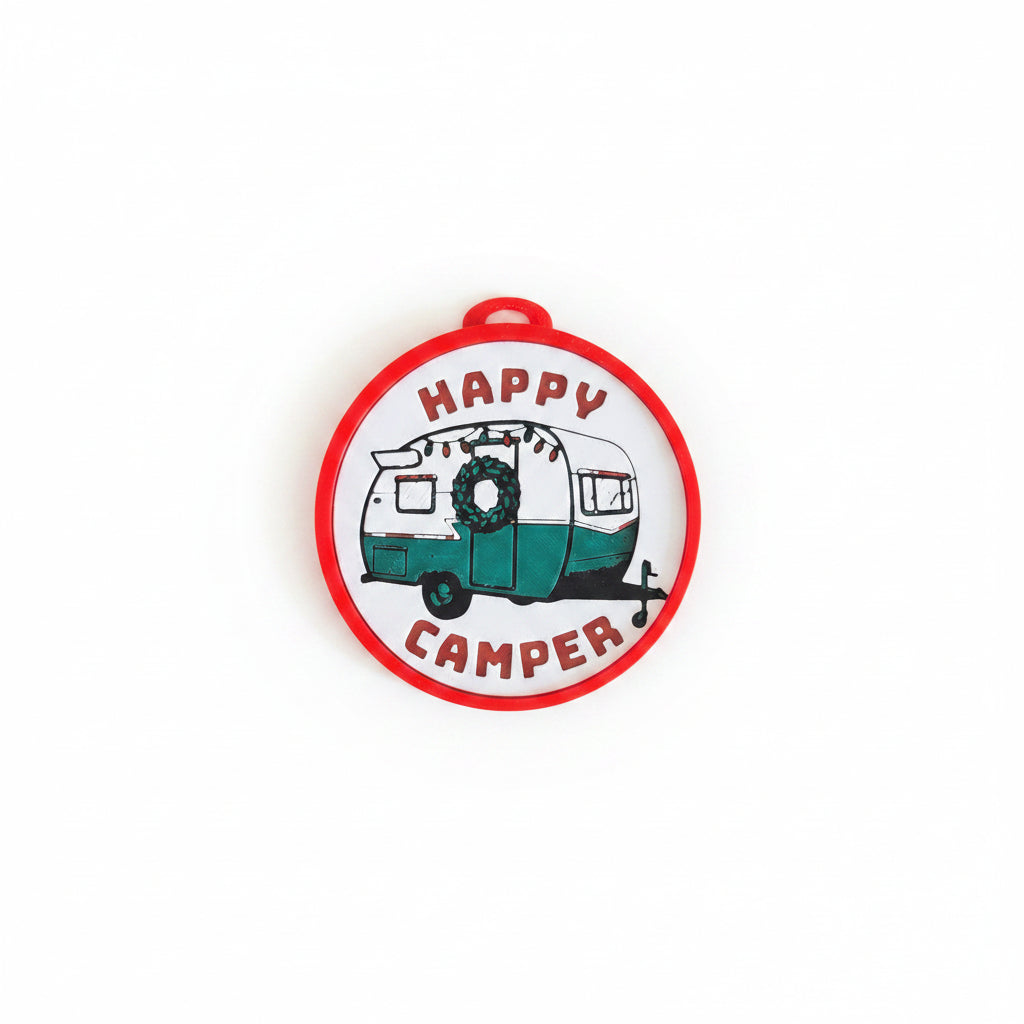 A round decorative 3D printed Christmas Ornament featuring a retro camping trailer illustration with the words 'HAPPY CAMPER' in red text, shown against a white background.