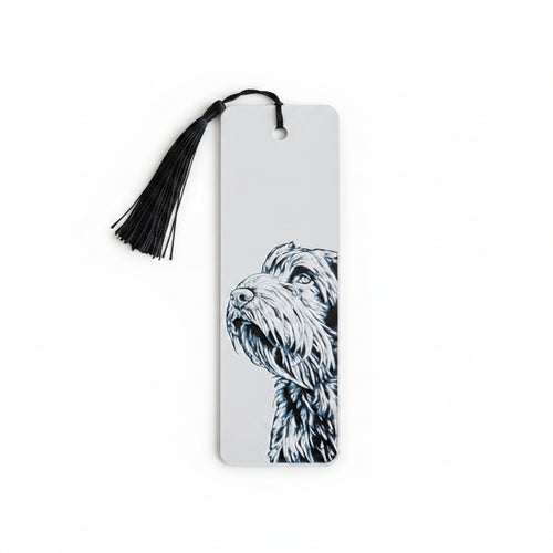 A white rectangular 3D printed bookmark with a black tassel at the top and a black-and-white illustration of a handsome scruffy dog on the right side, photographed against a light beige textured background.